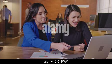 Senior business female executive looking at graphs and results with younger female staff at office workplace. Business woman coaching employee Stock Photo