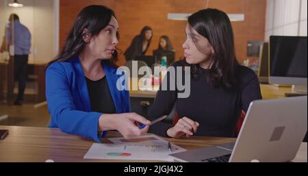 Senior business female executive looking at graphs and results with younger female staff at office workplace. Business woman coaching employee Stock Photo