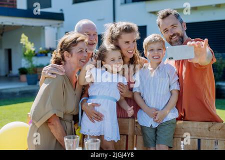 Multi generation family taking selfie on backyard in summer during garden party Stock Photo