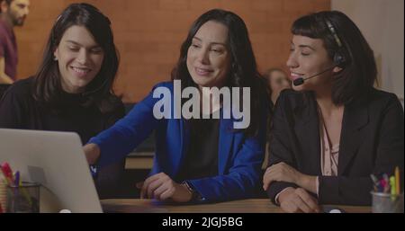 Business woman coaching younger staff in front of computer laptop. Female leader explaining protocol to staff wearing headsets at office Stock Photo