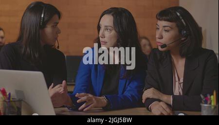 Business woman coaching younger staff in front of computer laptop. Female leader explaining protocol to staff wearing headsets at office Stock Photo