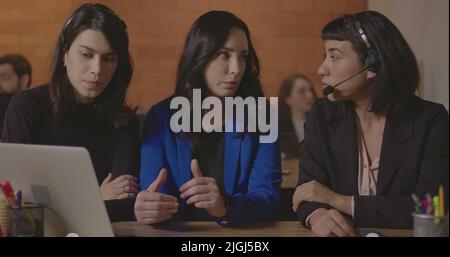 Business woman coaching younger staff in front of computer laptop. Female leader explaining protocol to staff wearing headsets at office Stock Photo