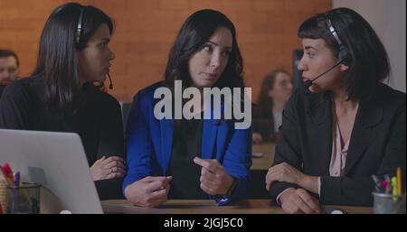 Business woman coaching younger staff in front of computer laptop. Female leader explaining protocol to staff wearing headsets at office Stock Photo