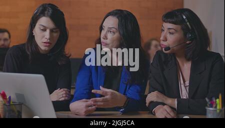 Business woman coaching younger staff in front of computer laptop. Female leader explaining protocol to staff wearing headsets at office Stock Photo