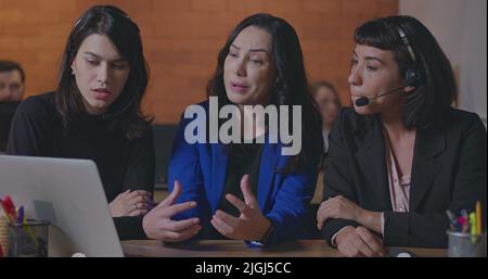 Business woman coaching younger staff in front of computer laptop. Female leader explaining protocol to staff wearing headsets at office Stock Photo