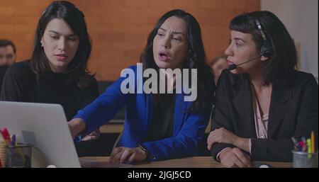 Business woman coaching younger staff in front of computer laptop. Female leader explaining protocol to staff wearing headsets at office Stock Photo