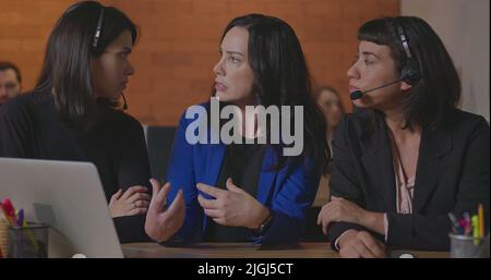 Business woman coaching younger staff in front of computer laptop. Female leader explaining protocol to staff wearing headsets at office Stock Photo