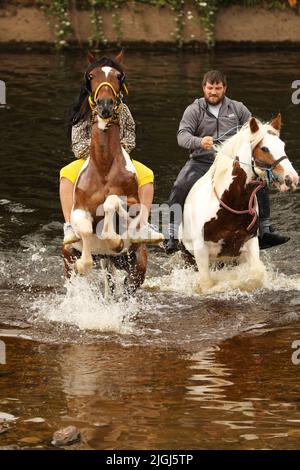 A young man and woman riding their horses through the River Eden, Appleby Horse Fair, Appleby in Westmorland, Cumbria
