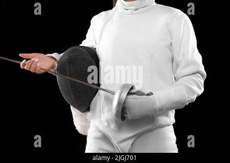 Closeup female fencer's body in white fencing costume with mask and rapier isolated on dark background. Sport, youth, activity, skills, achievements Stock Photo