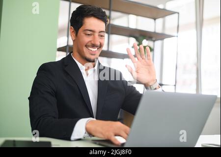 Young latin businessman entrepreneur in business wear talking online, discussing project, gesturing, presenting new business idea to client, team or to investor online on video call via laptop Stock Photo