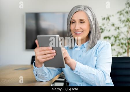 Smiling mature businesswoman sit in office and using digital tablet Stock Photo