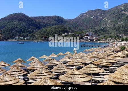 View to azure bay and beach hotels surrounded by green mountains. Summer resort with wicker parasols and lounge chairs in Mediterranean sea Stock Photo