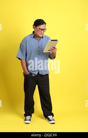 The adult Asian man with blue shirt standing on the yellow background. Stock Photo