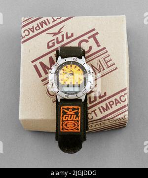 Armbandsur Brace watch in ASK. Around steel with four knobs and marking 0-60. Yellow dial with red numbering. Three black handers, hour and minute hand with luminous function. Text in black on the dial: "Yellow Quartz Japan Mov´t". Around the yellow dial is a black ring with markings in white. Below the dial is rectangular box for digital time indication. Under the box is the text: "Water Resist". Bracelet in black elastic with Velcro. On the bracelet a black gum plate with text in orange: "yellow". The watch is located in square cardboard with text in burgundy: "Yellow Impact Chrome". In the Stock Photo