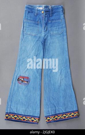 Jeans Boy pants. Jeans in denim, cotton. Waist pants with flared legs. Zipper gold. Linning with buttonholes and button in yellow metal in the middle. 6 pieces for belt. Square -sewn pockets. Yellow decorative seams. Switched decor straps on the bottom of the legs. Patterned woven ribbon geometric pattern in yellow/orange against blue bottom. On the right leg pasted team patch with machine-sewn red text "Grand Prix" and Formula 1 car in red, white, black. Size: C 125. (Marking The Waist Inside) Waist width 270 mm, Benvidd 230 mm. Appeal by Morgan Olsson, Swan Hall 2014 by Morgan Olsson, Svanha Stock Photo