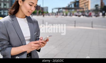 Young Asian business woman using smartphone on city street outdoors. Stock Photo