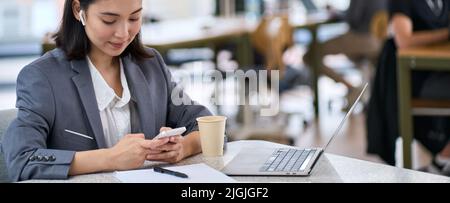 Young Asian business woman using smartphone at work. Banner Stock Photo
