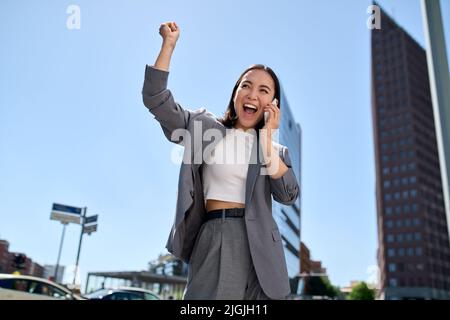 Young cheerful Asian businesswoman talking on cellphone laughing on city street. Stock Photo