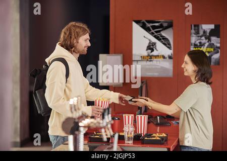 Young man pying with credit card fr his popcorn while seller holding terminal at counter Stock Photo