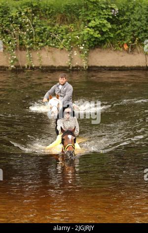 A young man and woman riding horses through the River Eden, Appleby Horse Fair, Appleby in Westmorland, Cumbria Stock Photo