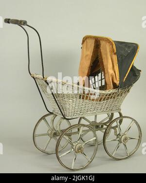 Dockvagn Doll wagon with braided basket 43 x 25 cm. With sheets, pillowcases, quilt, mattress and pillow. Suflett black painted. The cord brown with fringes, snowmaker. Basket gray painted. Undercut gray painted with black decor lines on wheels. Steel board with black stained, turned handle. Bed textiles: the lower sheets 43.5 x 29, upper litter 53 x 30, pillowcase with 3 pages 17 x 27, blanket white beige with pink edge 29 x 25, 1 blue mattress, 2 blue pillows. Gift 1973-02 by bakery master K-I. Eklöf. Admiralty g. 9. Karlskrona. The objects from the father's farm museum. Neg no: A 25453 Stock Photo