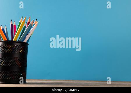 Image of cup of crayons on wooden table over blue background Stock Photo