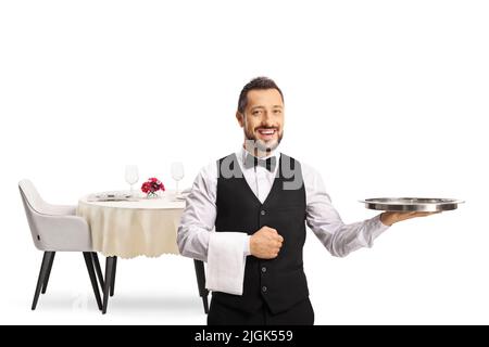 Full length portrait of a smiling server holding a tray and standing in front of a table isolated on white background Stock Photo
