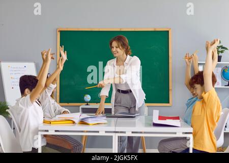 Smiling school teacher asks questions during lesson with group of happy children Stock Photo