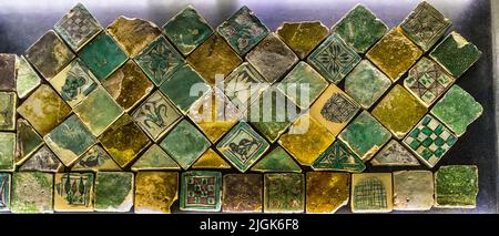 Green and yellow glazed floor tiles from the 14th century lie diagonally arranged in a display case in the Papal Palace of Avignon, France. The geometric and floral patterns come from the palace's original floors. Stock Photo