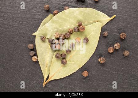 Dry fragrant black pepper and dry bay leaf on a slate stone, close-up, top view. Stock Photo