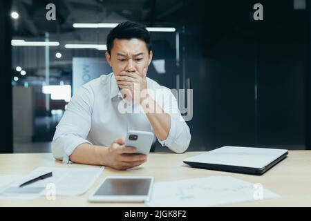 Businessman shocked read bad news from phone, asian boss in office reading online messages from phone Stock Photo