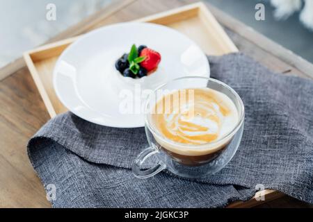 Pavlova dessert mini cake nest and a cup of latte coffee on the wooden tray with gray napkin on the table. Coffee time. To take a break and relax. Sel Stock Photo