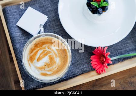 Cup of coffee, Pavlova dessert cake, gerbera flower and blank postcard with copy space on the tray with gray napkin. Breakfast for loved one. Romantic Stock Photo