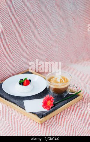 Cup of coffee, Pavlova dessert cake, gerbera flower and blank postcard with copy space on the tray with gray napkin. Breakfast for loved one. Romantic Stock Photo