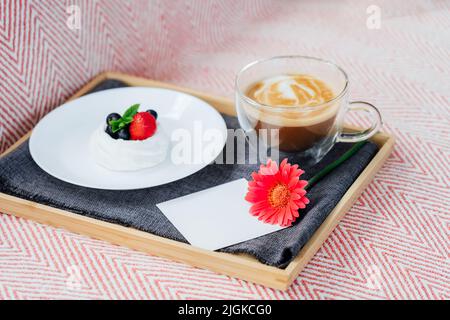 Cup of coffee, Pavlova dessert cake, gerbera flower and blank postcard with copy space on the tray with gray napkin. Breakfast for loved one. Romantic Stock Photo