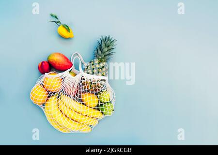 Top view string bag, mesh bag, grocery bag with organic fresh exotic fruits spilling from a reusable shopping bag on light blue background. Zero waste Stock Photo