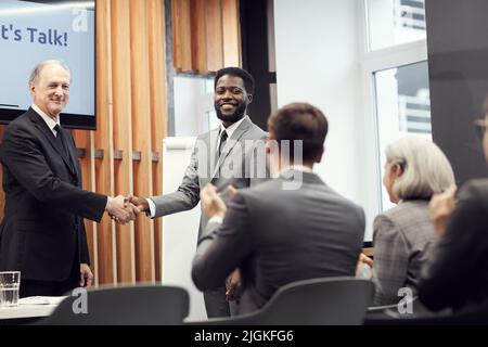 Company staff applauding while welcoming new Afro-American manager at company meeting, senior executive shaking his hand Stock Photo