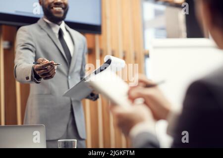 Close-up of black business speaker in suit standing in convention center room and gesturing hand at participant while responding positively to his ide Stock Photo