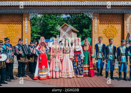 Kazan, Russia. June 19, 2022. Celebration of Sabantuy. A folk Tatar and Bashkir festival of field work. Men and women in national Tatar costumes at the gate of a traditional wooden house. Stock Photo