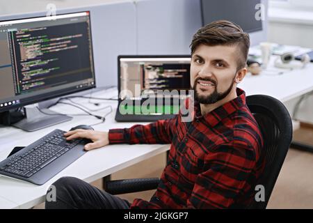 Computer programmer developer working in IT office, sitting at desk and coding, working on a project in software development company or startup. Stock Photo