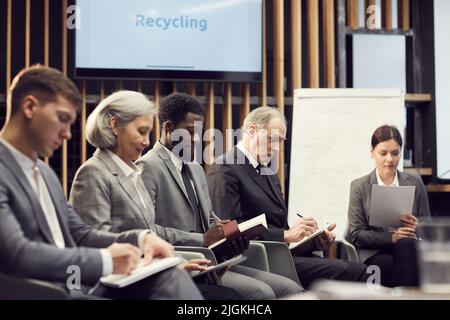 Group of content multi-ethnic business people in formal outfits sitting in line and making notes while performing creative task at training class Stock Photo