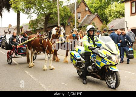 A police motorbike and two horses pulling traps along the road, Appleby Horse Fair, Appleby in Westmorland, Cumbria Stock Photo