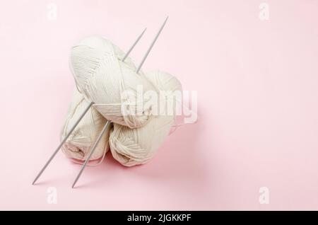 Light beige knitting wool and knitting needles on pastel pink background. Female hobby knitting. Soft woolen yarns for knitting warm clothes Stock Photo