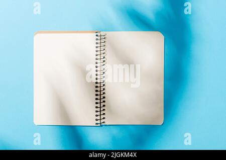 Blank notebook mockup with shadow of leaves on blue background. Elegant modern template for branding identity. Minimal nature background for summer co Stock Photo