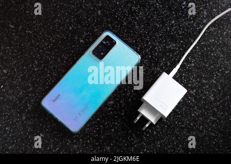 Redmi 10 mobile phone and charger on a black surface. Device with trendy color. Russia, Anapa-06,07,2022 Stock Photo