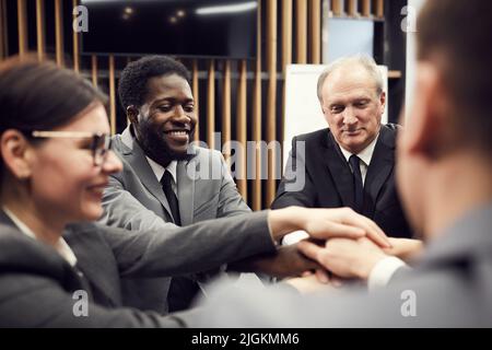 Group of positive excited multi-ethnic business colleagues standing in circle and stacking hands while enjoying teamwork Stock Photo