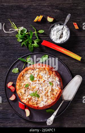 gluten free swiss rhubarb pie, rhabarberwahe, sprinkled with sliced almonds and icing sugar on black platter with fresh rhubarb on black stone board o Stock Photo