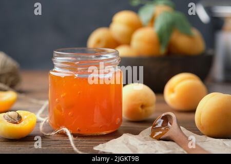 Jar of homemade apricot jam and ripe apricot fruits on kitchen table. Stock Photo