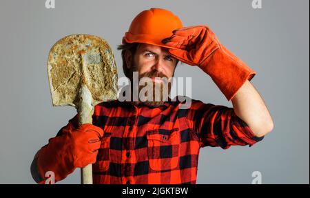Smiling builder in hard hat with shovel. Workman in work gloves with spade. Building and repair. Stock Photo