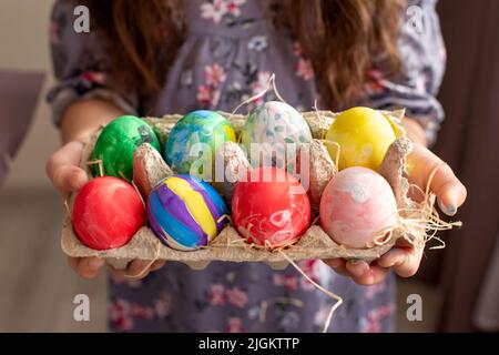 Hands of a girl in a dress holding a cardboard tray with colorful hand-painted eggs Stock Photo